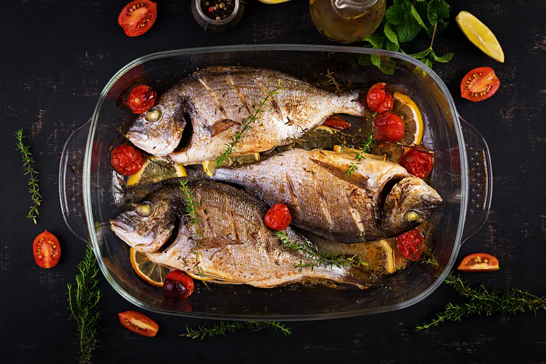 Whole fish baked with cherry tomatoes and herbs in a glass dish