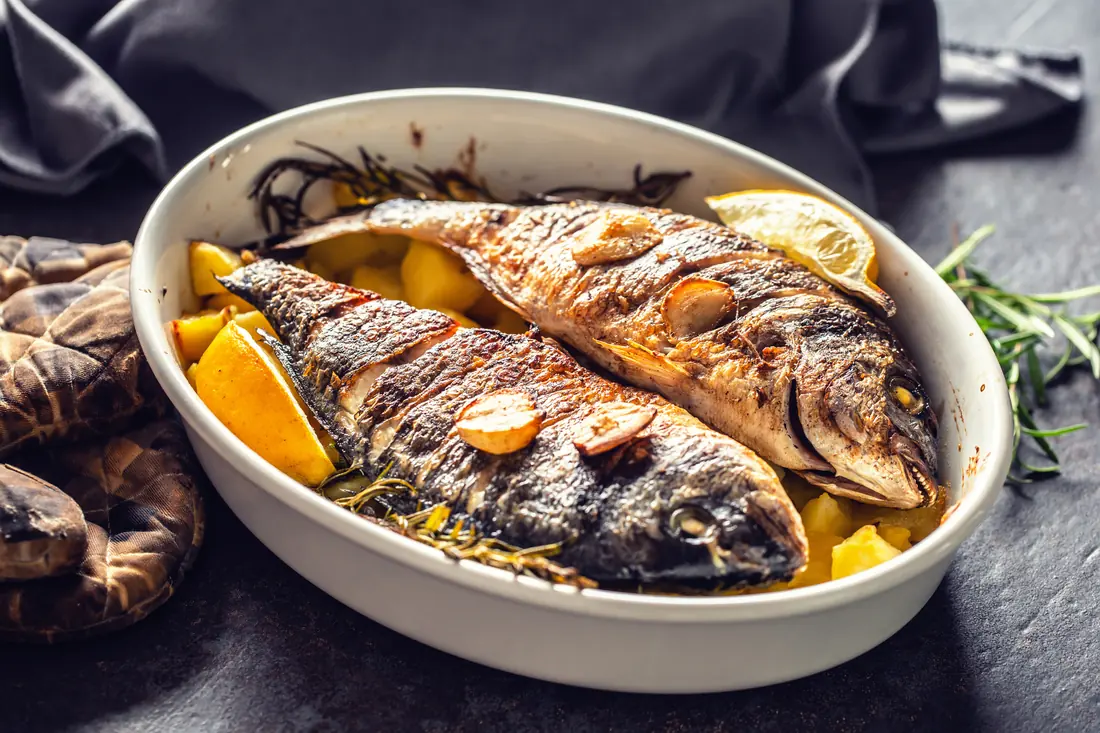 Whole roasted sea bream with lemon, rosemary and potatoes in a dish