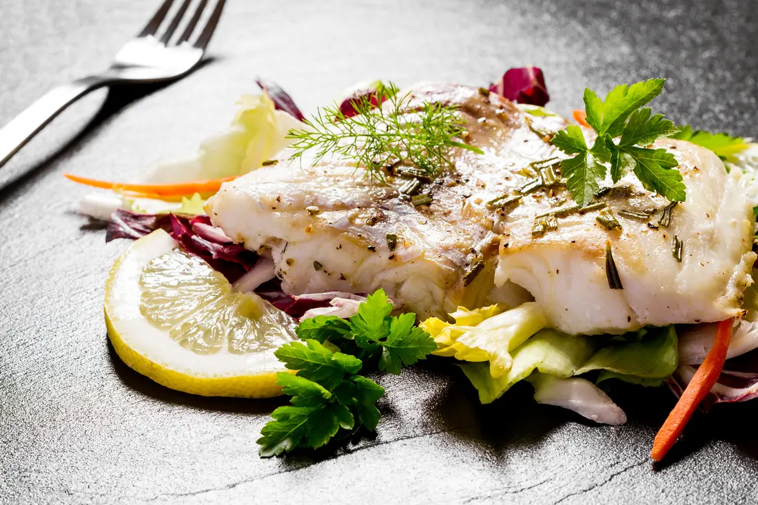 Cod fillet with herbs, lemon and salad on a slate