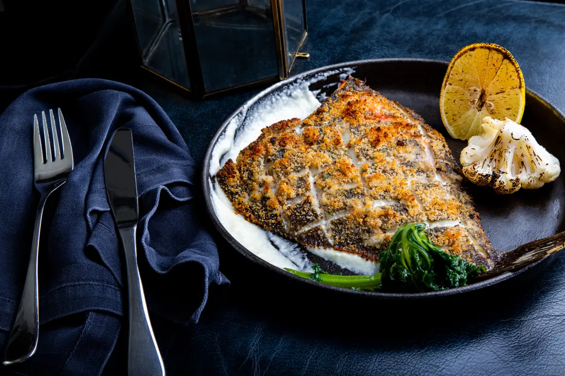 Roasted flat fish with lemon and herbs in a dark pan